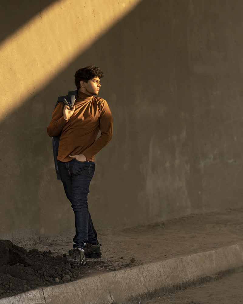 Shubhankar in a rust shirt leaning against a concrete wall in golden light