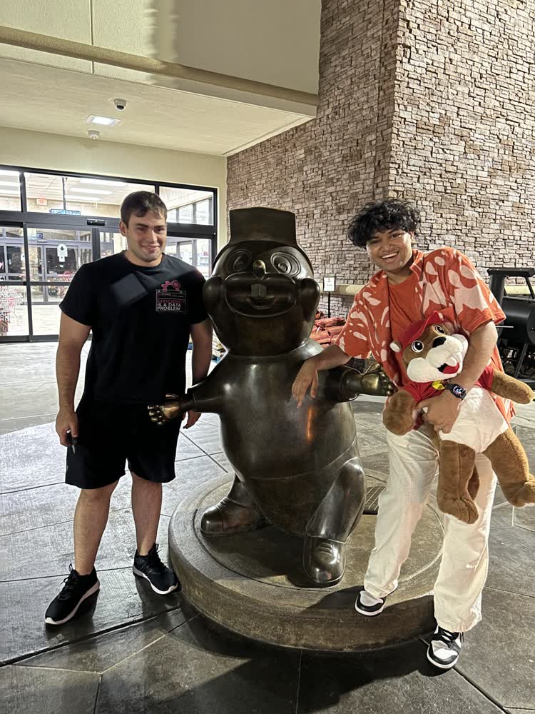 Shubhankar and a friend with the bronze beaver statue at Buc-ee’s, holding a plush beaver