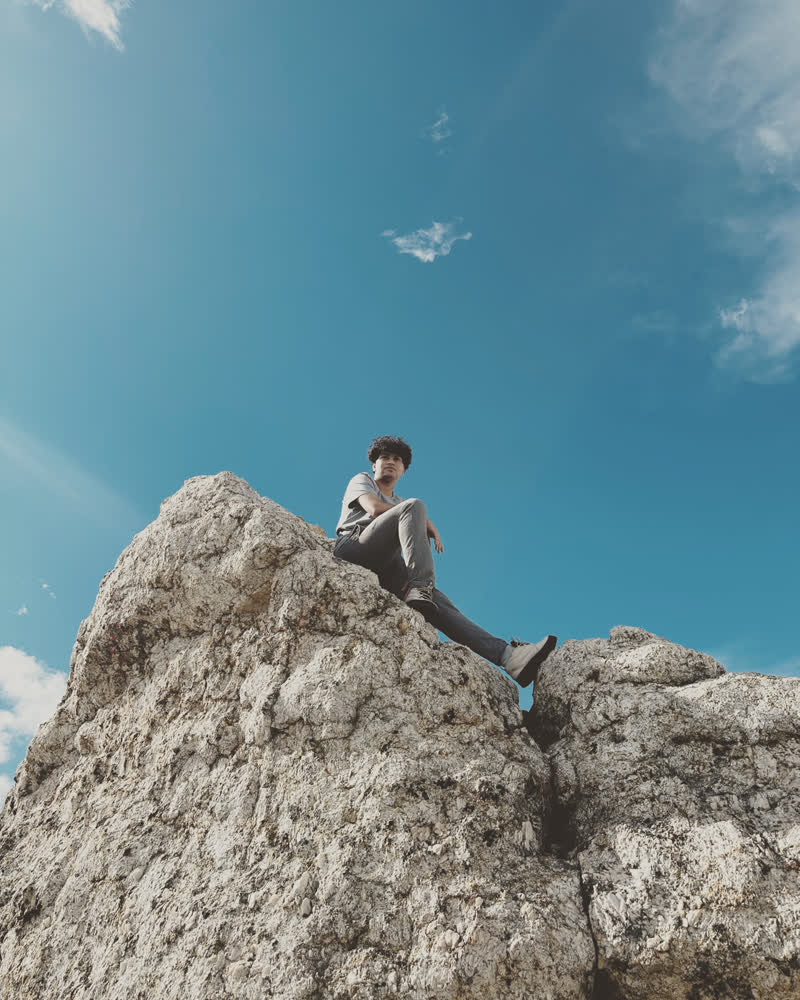 Shubhankar sitting on top of a boulder against a blue sky