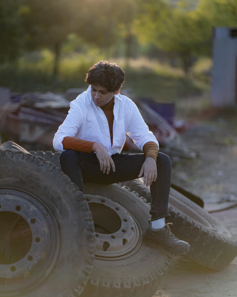 Shubhankar in a white shirt sitting on a stack of old tyres