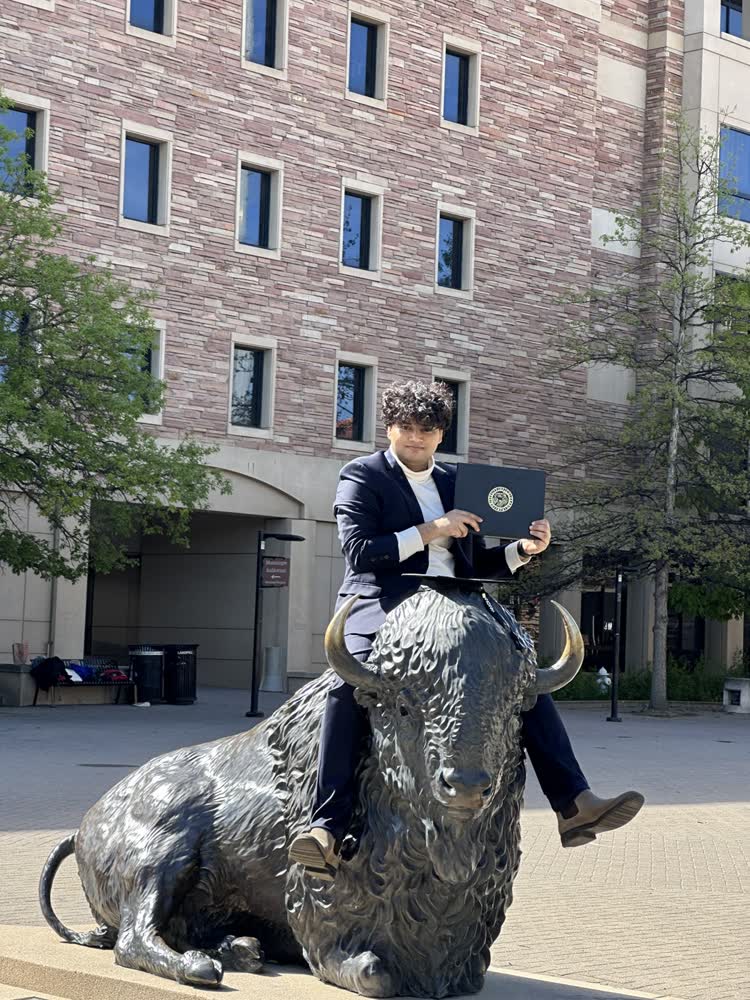 Shubhankar in a suit sitting on the bronze buffalo statue at CU Boulder